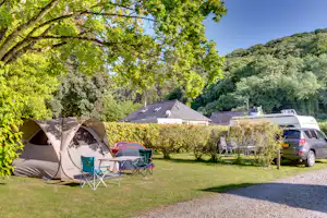 Campingzelt im Garten neben einem Stellplatz mit Wohnmobil und Auto, umgeben von Bäumen und Hecken.