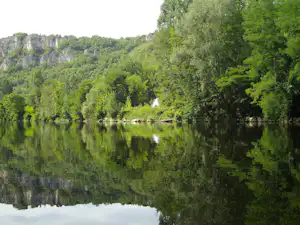 Ruhiger See mit Spiegelung, umgeben von dichtem Wald und Felsen am Ufer.