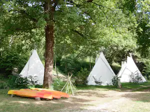 Drei weiße Tipis auf einem Campingplatz im Grünen, mit bunten Liegen und Bäumen im Hintergrund.