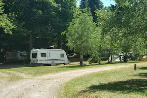 Wohnmobil auf einem Campingplatz im Grünen, mit Vorzelt, Zelt und weiteren Fahrzeugen zwischen Bäumen.