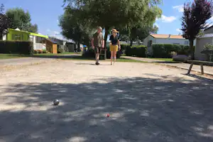 Campinganlage mit zwei Personen, Rasenfläche, Bäumen und Reihen von Mobilheimen, im Hintergrund ein Weg und Hecken.
