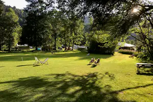 Campingwiese mit Wohnwagen und Zelten, Sitzstühlen und Picknicktisch unter Bäumen, im Hintergrund Berge.