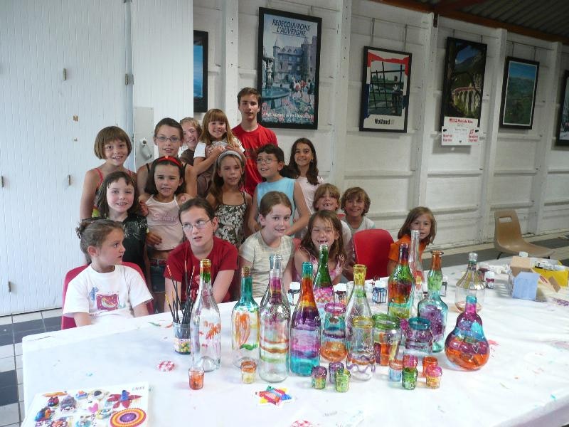 Kindergruppe vor einer weißen Wand und Galerie, an einem Tisch mit vielen bunten Getränkeflaschen.