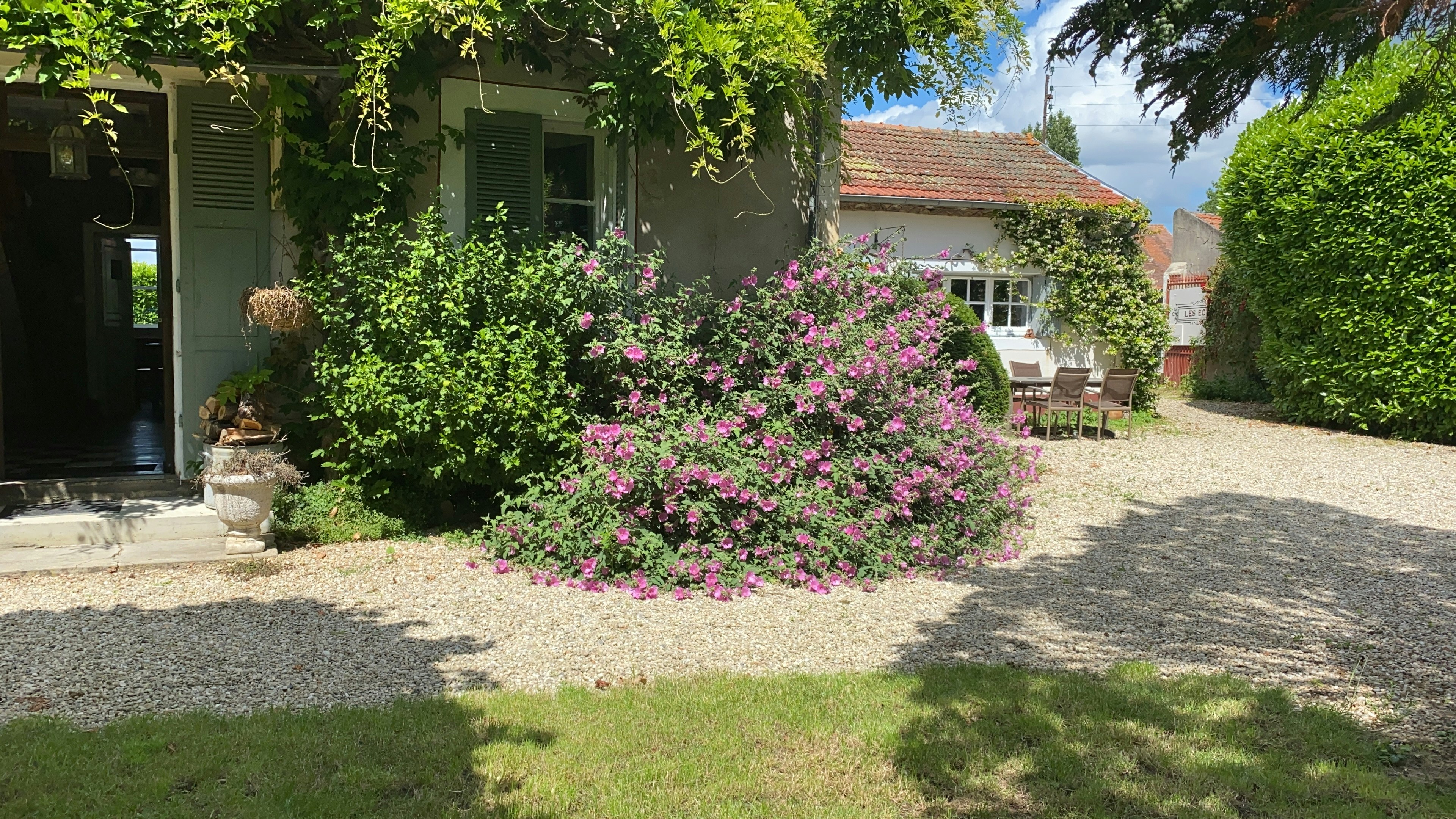Haus am Campingplatz mit blühendem Blumenbeet, Kiesweg und grünen Büschen vor der Terrasse.