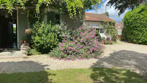 Haus am Campingplatz mit blühendem Blumenbeet, Kiesweg und grünen Büschen vor der Terrasse.