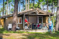 Camping Les Embruns - Mobilheim mit überdachter Veranda zwischen Bäumen