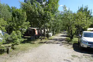 Campingplatz mit Zelt und Sitzgruppe unter Bäumen, Kiesweg und geparktem Auto am Stellplatz.