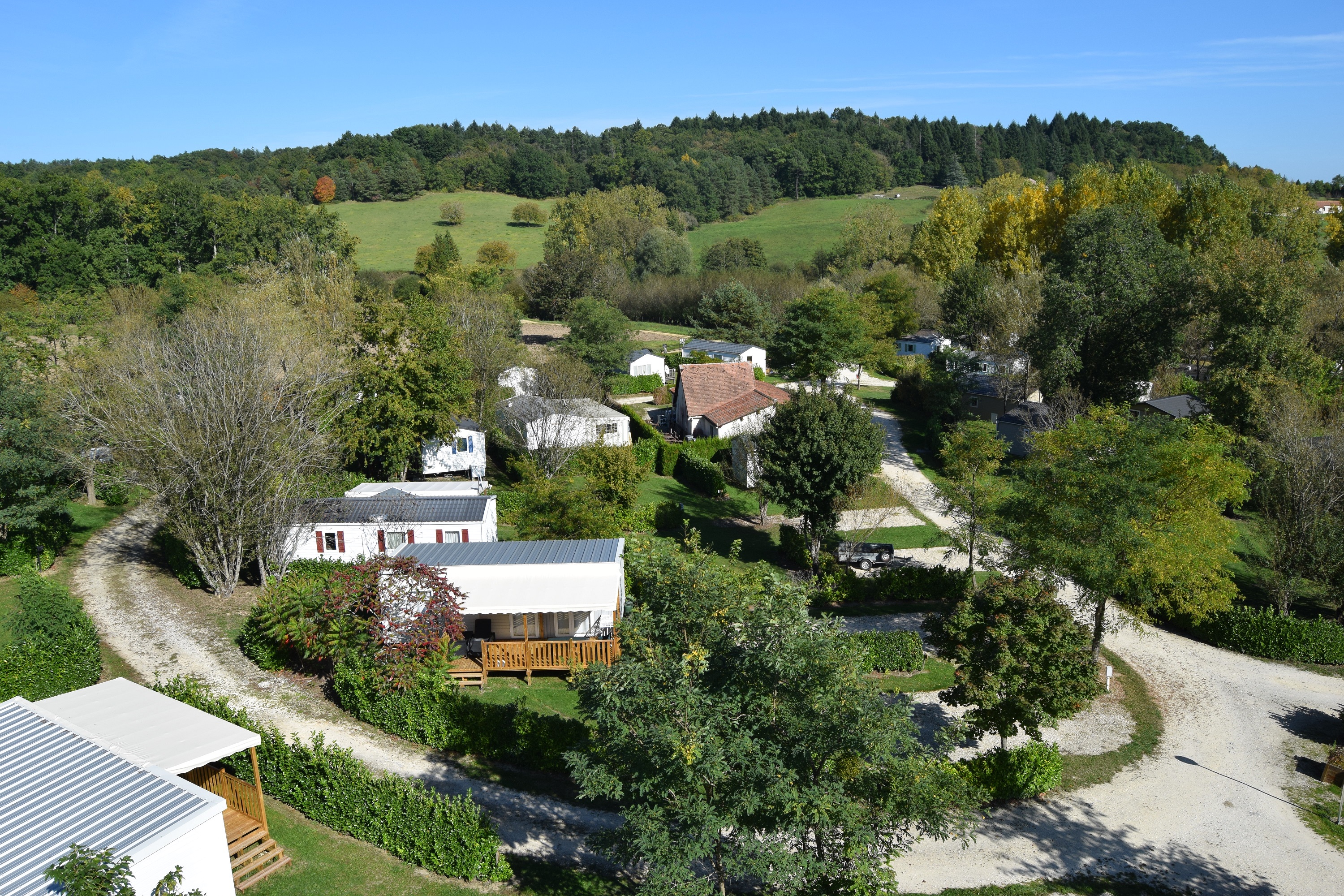 Campinganlage im grünen Tal mit mehreren Gebäuden, Wegen und viel Grün umgeben von Hügeln und Bäumen.