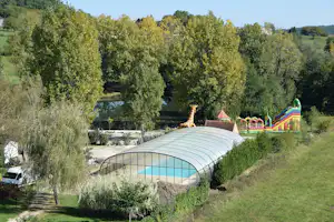 Überdachte Zeltkonstruktion auf einer Wiese, dahinter Bäume und ein Spielplatz mit Rutsche und bunten Elementen.