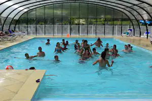 Beheiztes Schwimmbecken im Campingbereich mit vielen Badegästen, Glasdach und Liegen am Beckenrand.