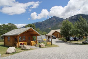 Camping Les Eygas - Blockhütte auf dem Campingplatz mit überdachter Veranda mit den Bergen der französischen Alpen im Hintergrund