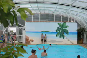 Überdachter Campingpool mit blauer Wasserfläche, Palmenwandbild und Kindern im Becken unter einem transparenten Dach.