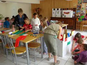 Familie beim Basteln an einem Tisch im Campinggebäude, Kinder mit Papier und Stiften, daneben Stühle und eine Theke.
