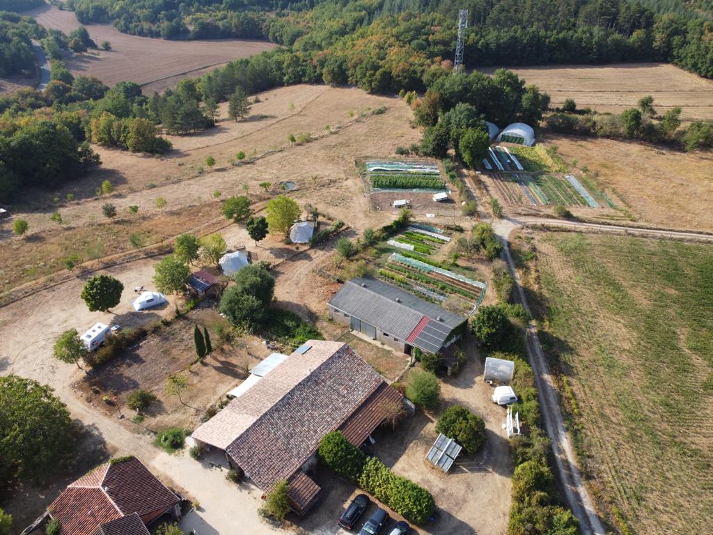Campinganlage im grünen Tal mit mehreren Stellplätzen, Wegen, kleinen Gebäuden und umgebenden Feldern und Bäumen.