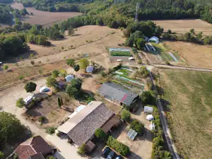 Campinganlage im grünen Tal mit mehreren Stellplätzen, Wegen, kleinen Gebäuden und umgebenden Feldern und Bäumen.