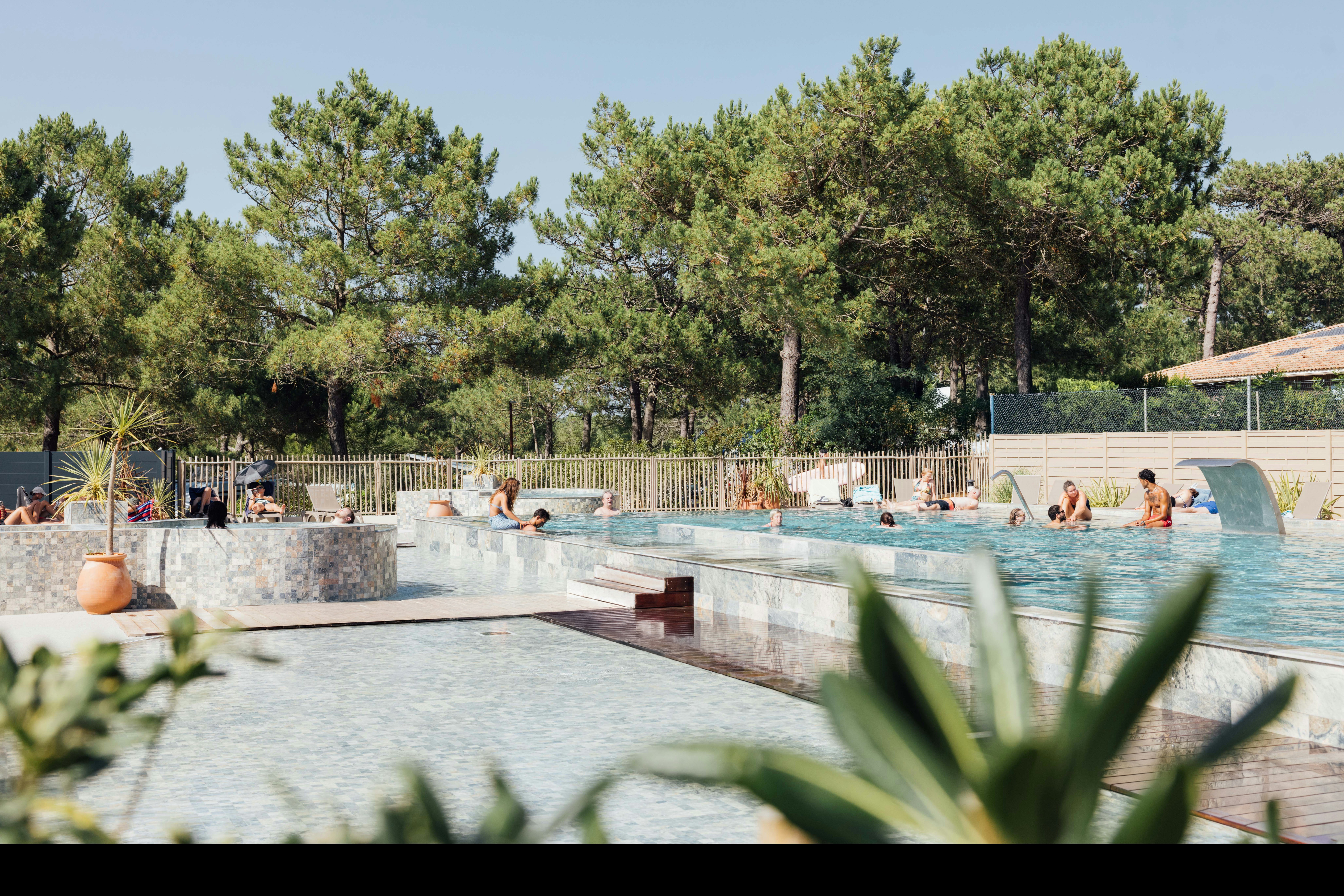 Schwimmbecken im Campingbereich mit mehreren Stufen, Liegen am Rand und Bäumen im Hintergrund.