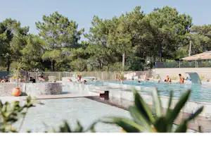 Schwimmbecken im Campingbereich mit mehreren Stufen, Liegen am Rand und Bäumen im Hintergrund.