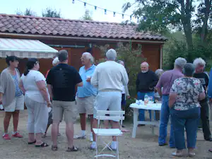 Gruppe von Campern auf einer Camping-Terrasse vor einem Holzhaus, mit Tischen und Stühlen im Hintergrund.