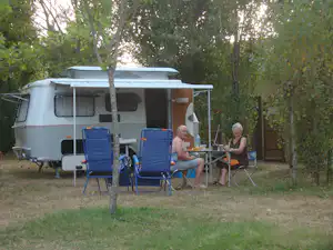 Wohnwagen mit Vorzelt und zwei Campingstühlen auf dem Stellplatz, im Hintergrund Bäume und ein Tisch.