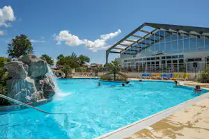 Großes Schwimmbecken mit türkisfarbenem Wasser, Sonnenterrasse und Liegen vor einem modernen Gebäudekomplex.