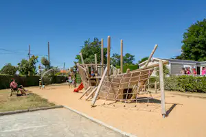Spielplatz auf dem Campingplatz mit hölzernem Klettergerüst, Sandboden und Hecken entlang des Weges.
