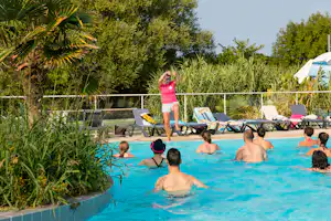 Kinder und Erwachsene im Camping-Pool, umgeben von Liegen, Palmen und dichtem Grün im Garten.