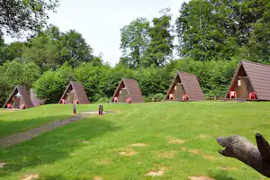 Mehrere Camping-Dachhütten mit roten Stühlen auf einer grünen Wiese, umgeben von Bäumen und einem Holzgeländer.