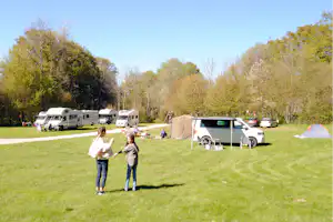 Wohnmobile und Zelte auf einem grünen Campingplatz, mit Wohnwagen, Picknicktisch und Stühlen am Stellplatz im Grünen.