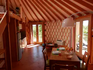 Innenansicht eines Wohnwagens mit Esstisch, Stühlen, Küchenzeile und großen Fenstern, rotem Stoffdach und Holzfußboden.