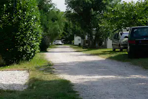 Schotterweg auf dem Campingplatz mit geparkten Autos, Bäumen und einem weißen Mobilheim mit Holzveranda.