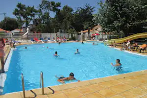 Camping Les Jardins de l'Atlantique - Pool vom Campingplatz mit Wasserrutsche und Liegestühlen in der Sonne, Spielplatz im Hintergrund