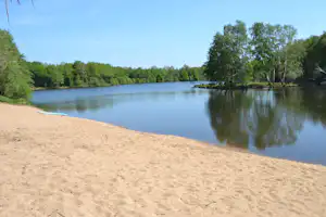 Ruhiger See mit Sandstrand, spiegelndem Wasser und Uferbäumen im Grünen, Blick über die Wasserfläche.