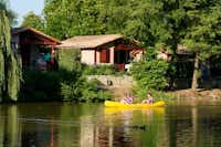 Camping Les Lacs de Courtès - Chalets mit Fluss davor, auf dem Kanufahrer fahren
