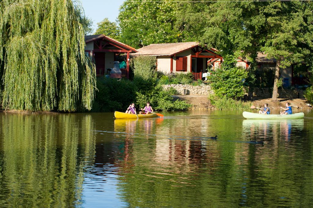 Ruhiger Fluss mit Ruderbooten, im Hintergrund Campinghäuser und Bäume am Ufer.