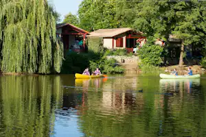 Ruhiger Fluss mit Ruderbooten, im Hintergrund Campinghäuser und Bäume am Ufer.