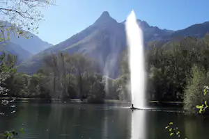 Wasserfall in einem See, umgeben von Bäumen und Bergen im Hintergrund, mit Blick auf das Tal.