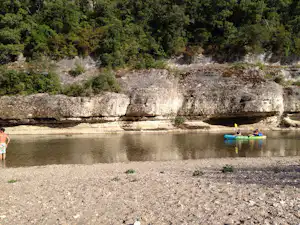 Ruhiger Fluss am Campingplatz mit Booten im Wasser und steiler Felswand am Ufer, umgeben von Bäumen.