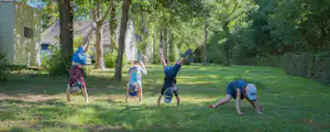 Kinder und Erwachsene machen Übungen im grünen Campinggarten, neben Wohnwagen und Bäumen auf dem Rasen.