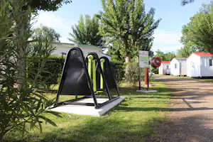 Spielgerät mit Rutsche auf dem Rasen am Campingplatz, daneben Bäume, Weg und Mobilheime mit weißen Wänden und roten Dächern.