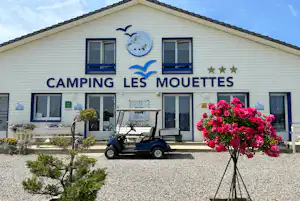 Vorderansicht eines Campinghauses mit Schriftzug „Camping Les Mouettes“, Blumenbeeten und Sitzbereich vor dem Gebäude.