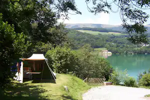 Zelt am Seeufer im Grünen, Rasenfläche und Weg, Blick auf ruhiges Wasser und bewaldete Hügel im Hintergrund.