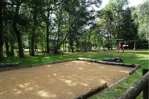 Sandkasten auf einem Campingplatz-Spielbereich, umgeben von Rasen, Bäumen und einem Spielgerät mit Schaukel.