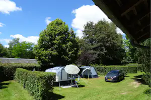 Zelte auf einem Campingplatz mit gepflegtem Rasen, Hecken und einem Auto neben dem Zeltbereich.