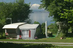 Campingzelt auf dem Stellplatz mit Blumen, umgeben von Bäumen, Blick auf den See und die Uferstadt in der Ferne.