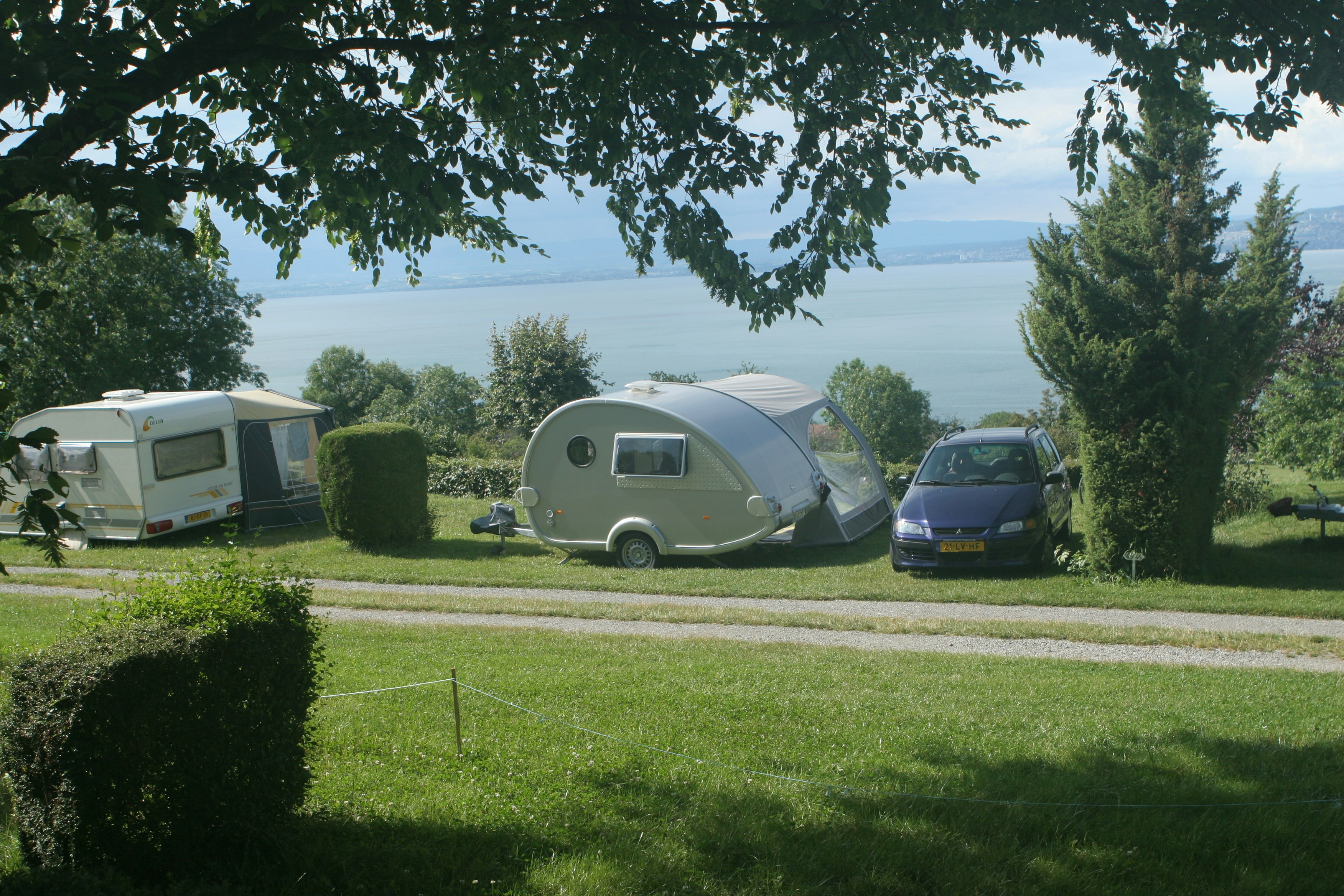 Camping Les Myosotis - Wohnwagenstellplatz zwischen Weg und See auf der Wiese der Campingplatzanlage