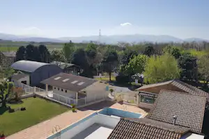 Blick auf Campinganlage mit Pool, Terrasse und Gebäuden, umgeben von Bäumen und grünen Feldern in den Hügeln.