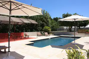 Pool auf der Camping-Terrasse mit Sonnenschirmen, Liegen und gepflastertem Boden, im Hintergrund Hecken und Zaun.