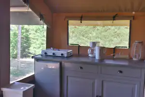 Campingküche im Zelt mit Gasgrill, Spüle, Kaffeekanne und Fenstern zum Blick in den Wald.