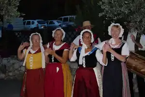 Gruppe in Trachten auf einem Campingplatz, im Hintergrund geparkte Autos und ein Zaun aus Holz.