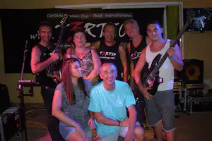 Band auf der Bühne mit Gitarren und Mikrofonen, mehrere Musiker posieren vor einer großen Konzertwand.